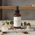 Velvet Clove Refining Mist amber bottle with botanical elements on white marble